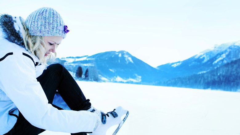 Ice skating on Lake Lunz, © weinfranz.at Person puts on ice skates on a snowy lake surrounded by mountains.