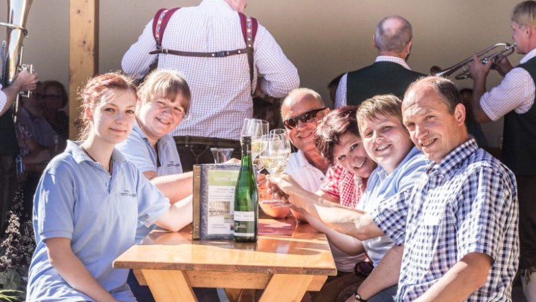 Geppel-Mayer family, © Winzerhof Geppel-Mayer Group of people sitting at an outdoor table, toasting with drinks.