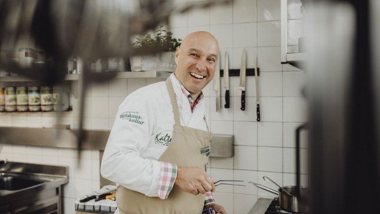 Wirt Hubert Kalteis, © Niederösterreich Werbung/Sophie Menegaldo Ein lachender Koch in einer professionellen Küche mit Messern an der Wand.