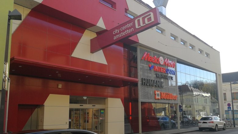 City Center Amstetten, © Roman Zöchlinger Eingang des City Center Amstetten mit roten und weißen Fassadenelementen und Schildern von Geschäften wie MediaMarkt und Müller.