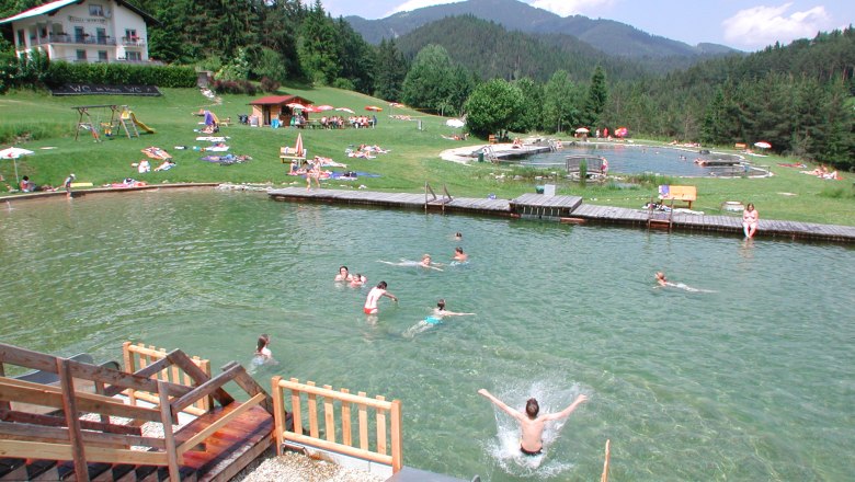 Gasthof Kalte Kuchl, © zVg Kalte Kuchl Menschen schwimmen in einem Naturbadesee mit umliegender Wiese und Wald.