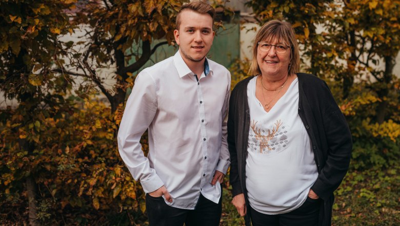 Always there for her guests: Brigitte Gürtler, © Niederösterreich Werbung/Daniela Führer A young man and an older woman stand smiling in front of autumnal trees.