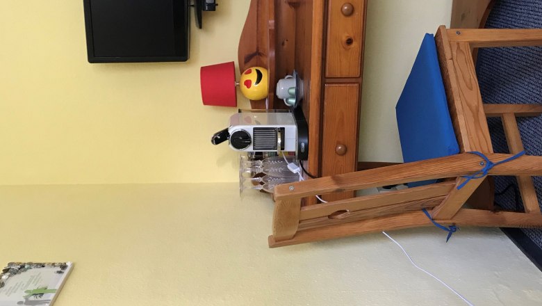 TDR House Maier Table, © Alicia Maier A small wooden table with a coffee machine, glasses, a lamp and a TV on the wall.