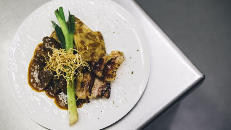 Roast beef from the Alpenvorland Beiried, © Niederösterreich Werbung/David Schreiber A plate with roast beef, potato gratin, leek and crispy onions on a metal surface.