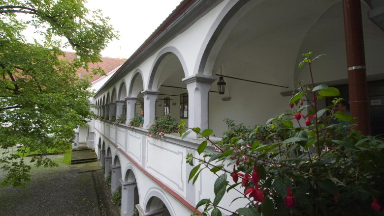 Schloss Scheibbs, © Dominik Stixenberger Ein zweistöckiger Arkadengang mit weißen Bögen und Blumen im Schloss Scheibbs.