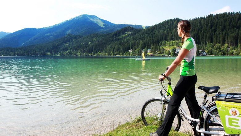 Türkisblaues Wasser am Erlaufsee, © weinfranz.at Frau mit Fahrrad am Ufer des Erlaufsees, umgeben von Bergen und Wald.