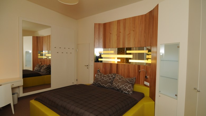 TDR Winery Haimel Rooms, © Weingut Haimel Modern bedroom with wood paneling and yellow bed.