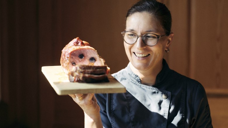 Das beliebteste Gericht von Wirtin Alexandra Hochholzer, © Niederösterreich Werbung/Julius Hirtzberger Eine Frau in Kochkleidung hält ein Holzbrett mit einem aufgeschnittenen Fleischgericht.
