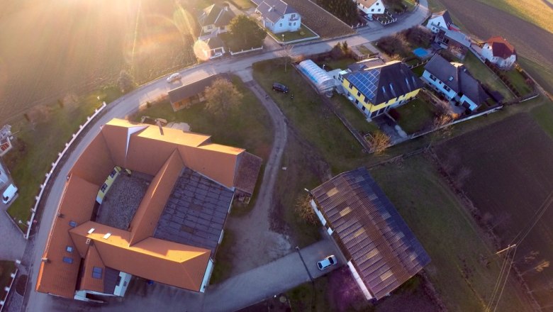 Luftansicht, © zur Verfügung gestellt: Weinbau Häusler Luftaufnahme eines Dorfes mit Häusern, Straßen und Feldern bei Sonnenuntergang.