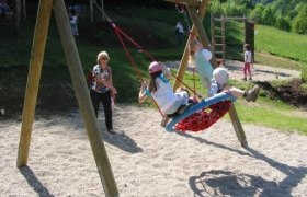 Spielplatz, © Bernhard Hofecker Kinder schaukeln auf einem Spielplatz in einer Nestschaukel.