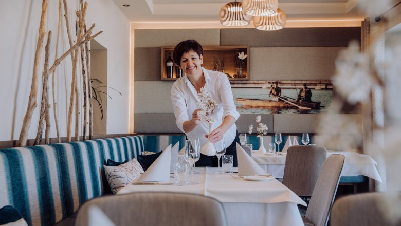 Wirtin Anneliese Harthaller kennt die Wünsche der Gäste, © Niederösterreich Werbung/thecreatingclick.com Eine Frau in einem Restaurant arrangiert Blumen auf einem Tisch.