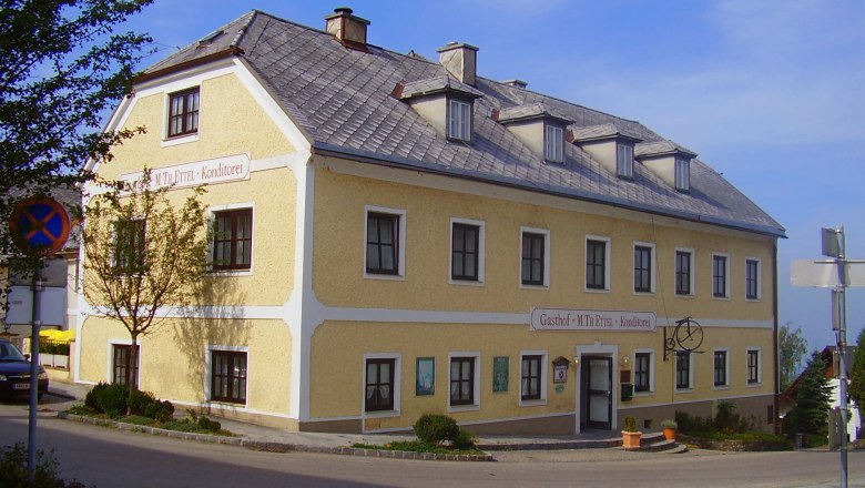 Gasthaus Ettel, © Gasthaus Ettel Gelbes zweistöckiges Gebäude mit der Aufschrift 'Gasthof M. Th. Ettel Konditorei'.