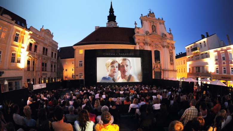 Cinema Paradiso, © Andrea Reischer/Cinema Paradiso Open-Air-Kinoabend auf einem Platz mit vielen Zuschauern vor einer großen Leinwand.