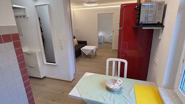 TDR-Haus Morgensonne Wohnzimmer, © Fam Pauker Kleines Wohnzimmer mit Esstisch, Stühlen, rotem Kühlschrank und Sofa.