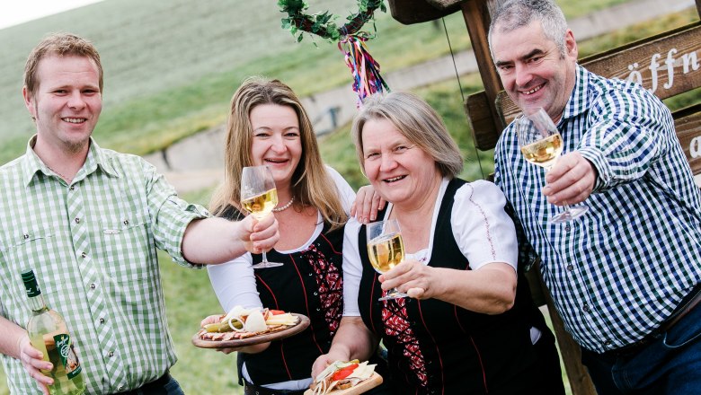 Mostheuriger z'Gridling, © schwarz-koenig.at Vier Personen stoßen mit Weingläsern an, im Freien vor einem Schild.