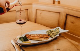 Zander in Knoblauchbutter, © Niederösterreich Werbung/Klaus Engelmayer Ein Teller mit Zanderfilet und Kartoffeln in Knoblauchbutter, daneben ein Glas Rotwein auf einem Holztisch.