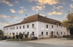 Landgasthof in Kilb, © Niederösterreich Werbung/David Schreiber Ein traditioneller Landgasthof mit Solarpanelen auf dem Dach und einem Schild vor dem Eingang, unter einem bewölkten Himmel.