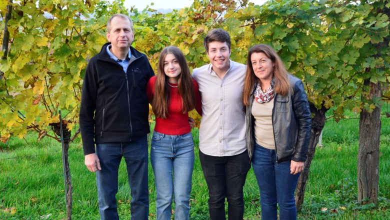 Poyntner family, © Familie Poyntner Four people stand smiling in front of vines outside.