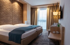 Das Alfred, © Niederösterreich Werbung / Maximilian Pawlikowsky Modernes Hotelzimmer mit Doppelbett, Holzverkleidung und Fenster mit Vorhängen.