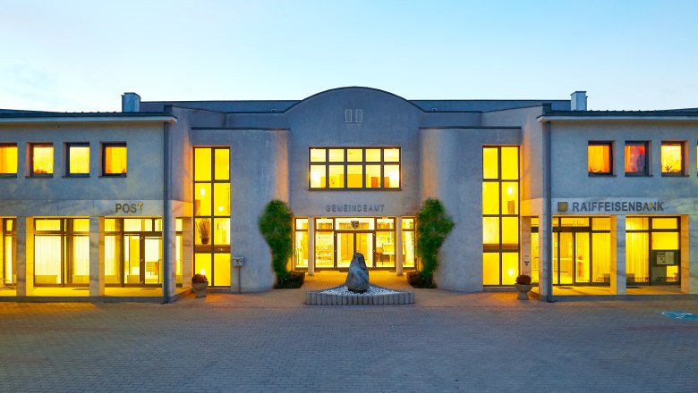 Obritzberg, © zVg Gemeinde Obritzberg-Rust Beleuchtetes Gebäude mit Aufschrift 'Gemeindeamt', 'Post' und 'Raiffeisenbank'.