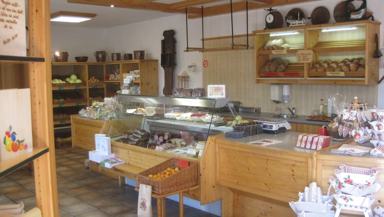 Farm store Lindenhof, © Danner Interior view of a farm store with wooden shelves filled with bread, fruit and sausage products.