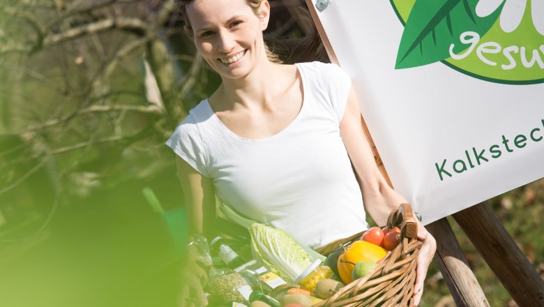 All-round healthy store, © schwarz-koenig.at Woman with a basket full of vegetables in front of a sign saying 'healthy'.