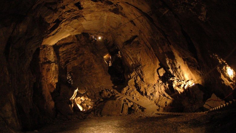 Hochkarhöhle, © Hochkar Bergbahnen GmbH Innenansicht einer beleuchteten Höhle mit steinigen Wänden und einem schmalen Pfad.