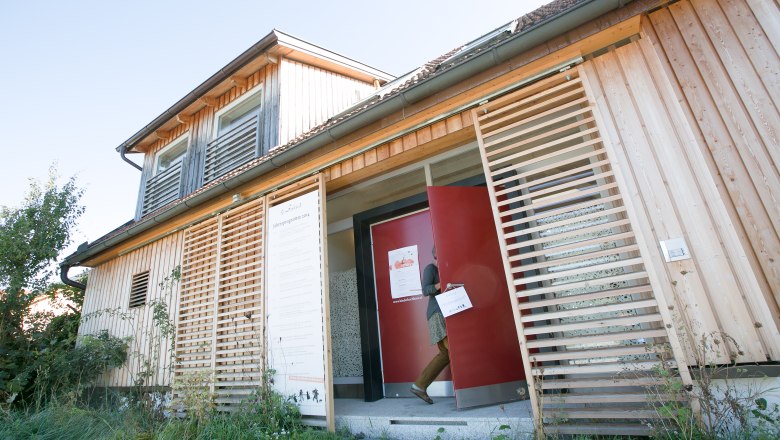 Tailor's cottage, © Doris Schwarz König A modern wooden building with a red door and a person entering the building.