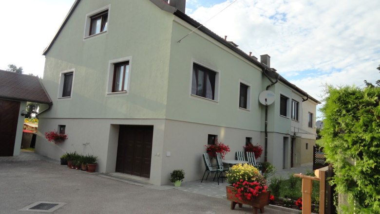 Hausansicht außen, © Schreiblehner Außenansicht eines zweistöckigen Hauses mit grünem Anstrich, Blumen und Gartenmöbeln im Vordergrund.