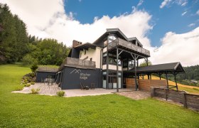 Ötscher Lodge, © Niederösterreich Werbung / Maximilian Pawlikowsky Ötscher Lodge in einer grünen, bewaldeten Umgebung mit blauem Himmel.