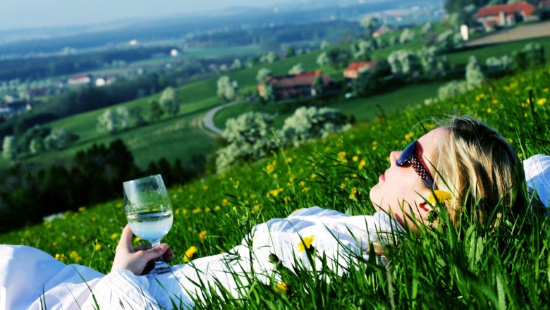 Gemeinde Weistrach, © Mostviertel Tourismus/Weinfranz.at Person liegt in einer Wiese mit einem Glas in der Hand, im Hintergrund eine hügelige Landschaft.