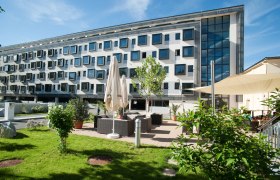 Das Gold´s, © Cityhotel DC Modernes Gebäude mit vielen Fenstern und Gartenbereich mit Sitzgelegenheiten.