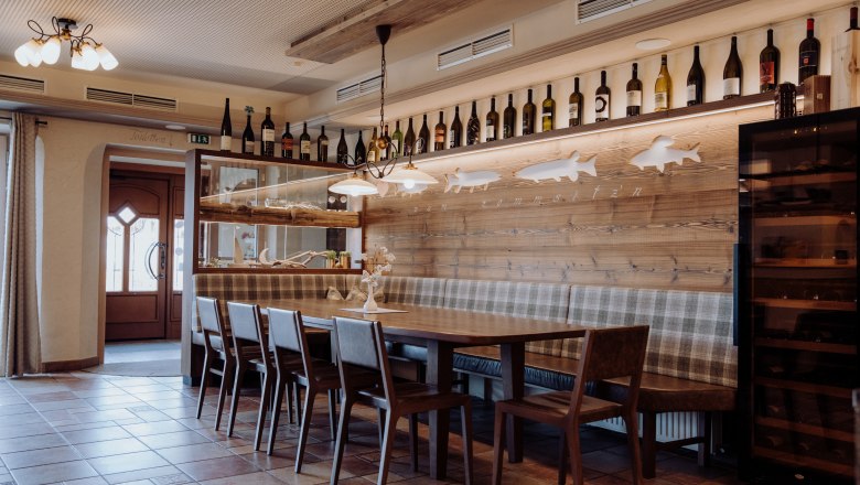 Hier fühlt man sich wohl, © Niederösterreich Werbung/thecreatingclick.com Gemütlicher Essbereich mit Holztisch, Stühlen und Bank, dekoriert mit Weinflaschen und Fischmotiven an der Wand.