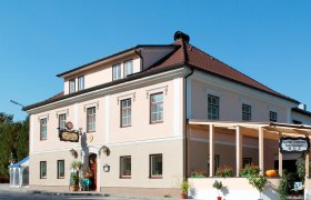 Schützenwirt, © zVg Ein traditionelles Gasthaus mit rosa Fassade und rotem Dach, dekoriert mit Pflanzen und einem Kürbis.