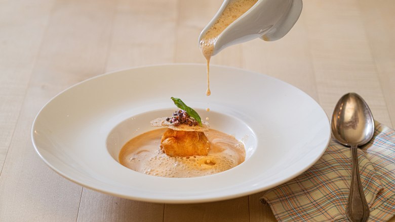 Traditional Mostviertel cuisine includes crayfish soup, © Niederösterreich Werbung/ Rita Newman Crab soup is poured into a plate, decorated with a dough ball and herbs.