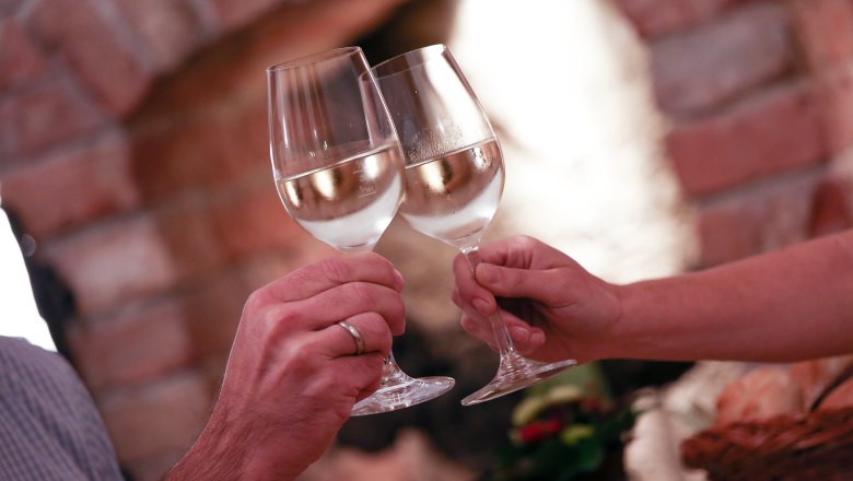 Weingläser, © Schwarz-König Zwei Personen stoßen mit gefüllten Weingläsern an.