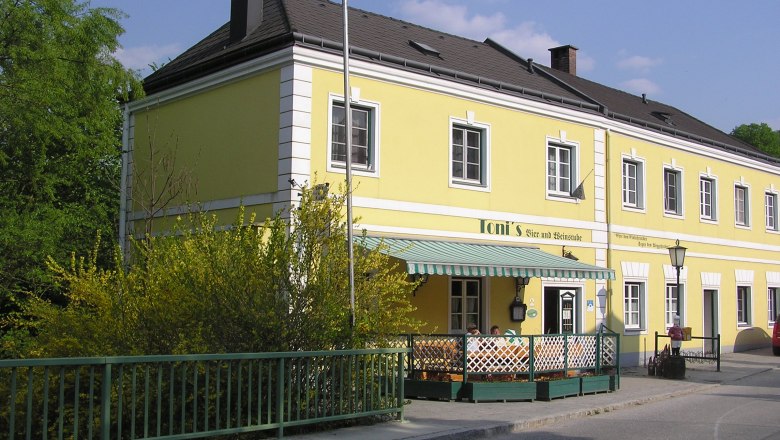 Toni's Bier- und Weinstube, © Toni's Bier- und Weinstube Gelbes Gebäude mit der Aufschrift 'Toni's Bier- und Weinstube', umgeben von grünen Pflanzen und einem Zaun.