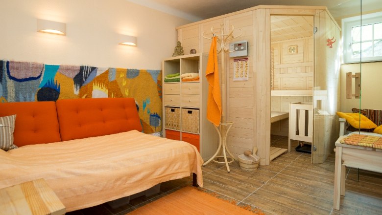 Ferienwohnung, © Reichlin Gemütliches Wohnzimmer mit Sauna, Sofa und bunter Wanddekoration.