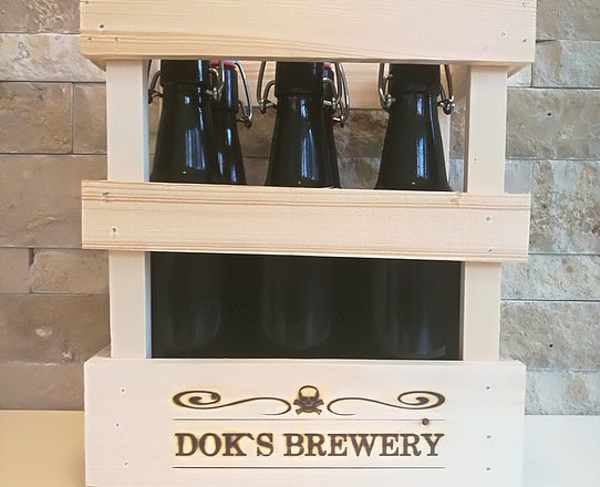 Bierauswahl, © Doks Brewery Holzkiste mit drei dunklen Bierflaschen von Dok's Brewery vor einer Steinwand.