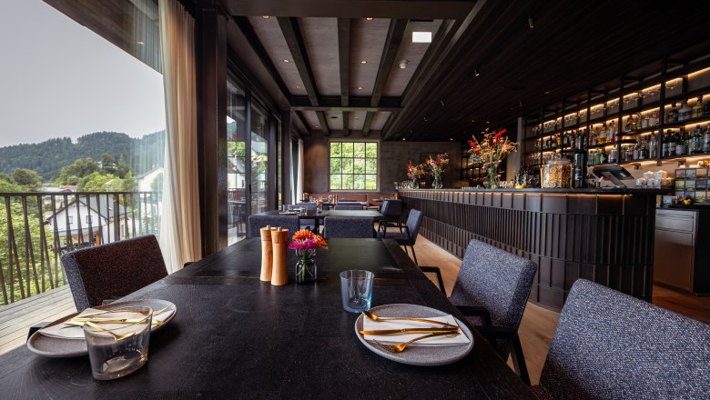 Refugium Lunz, © Niederösterreich Werbung / Maximilian Pawlikowsky Interior view of a modern restaurant with a set table and bar in the background.