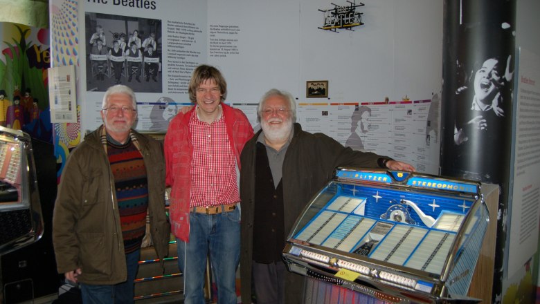 Pindigiland, © Pindigiland Three men stand in front of a Beatles exhibition with a jukebox.