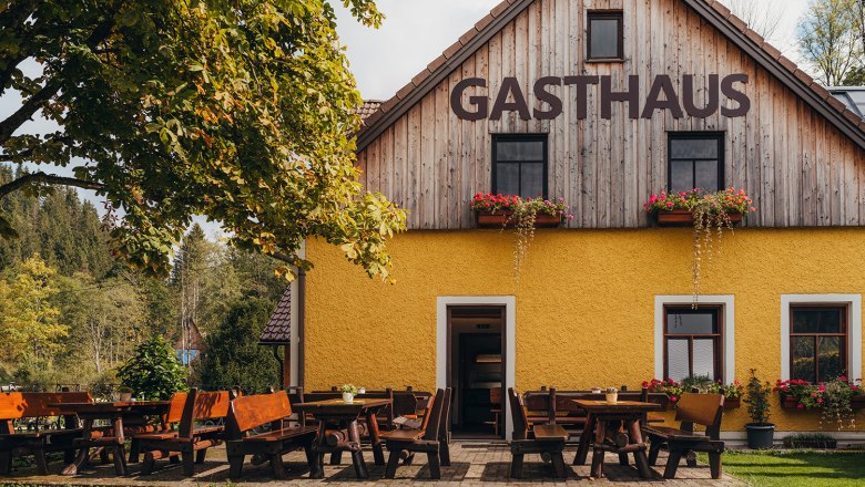 Located at the gateway to the Ötscher-Tormäuer Nature Park, © Niederösterreich Werbung/Daniela Führer A yellow inn with wooden tables and benches outside, surrounded by trees and nature.