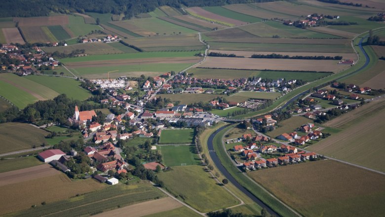 Luftaufnahme eines Dorfes mit umliegenden Feldern und einem Fluss.