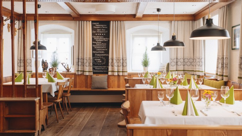 Gemütliche, traditionelle Gaststube mit Holzmöbeln, gedeckten Tischen und grünen Servietten.