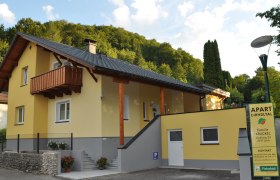 Gelbes Haus mit Balkon und Schild 'Apart Dirndltal' vor einem bewaldeten Hügel.