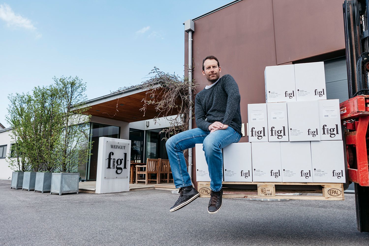 Ein Mann sitzt auf gestapelten Weinkartons vor dem Weingut Leopold Figl.
