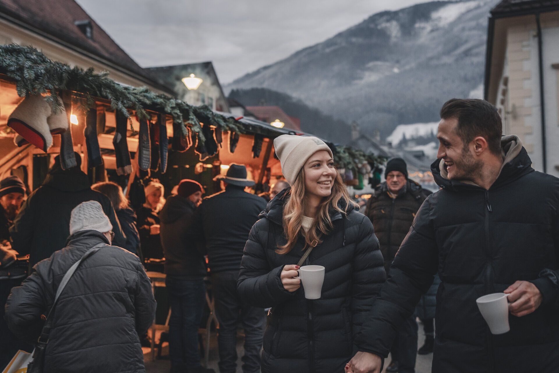 Pärchen schlendert über Adventmarkt mit Bergkulisse im Hintergrund. 