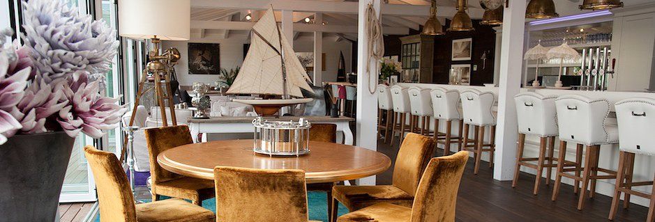 Eleganter Barbereich mit runden Holztischen, samtigen Stühlen und einer Bar mit weißen Hockern.