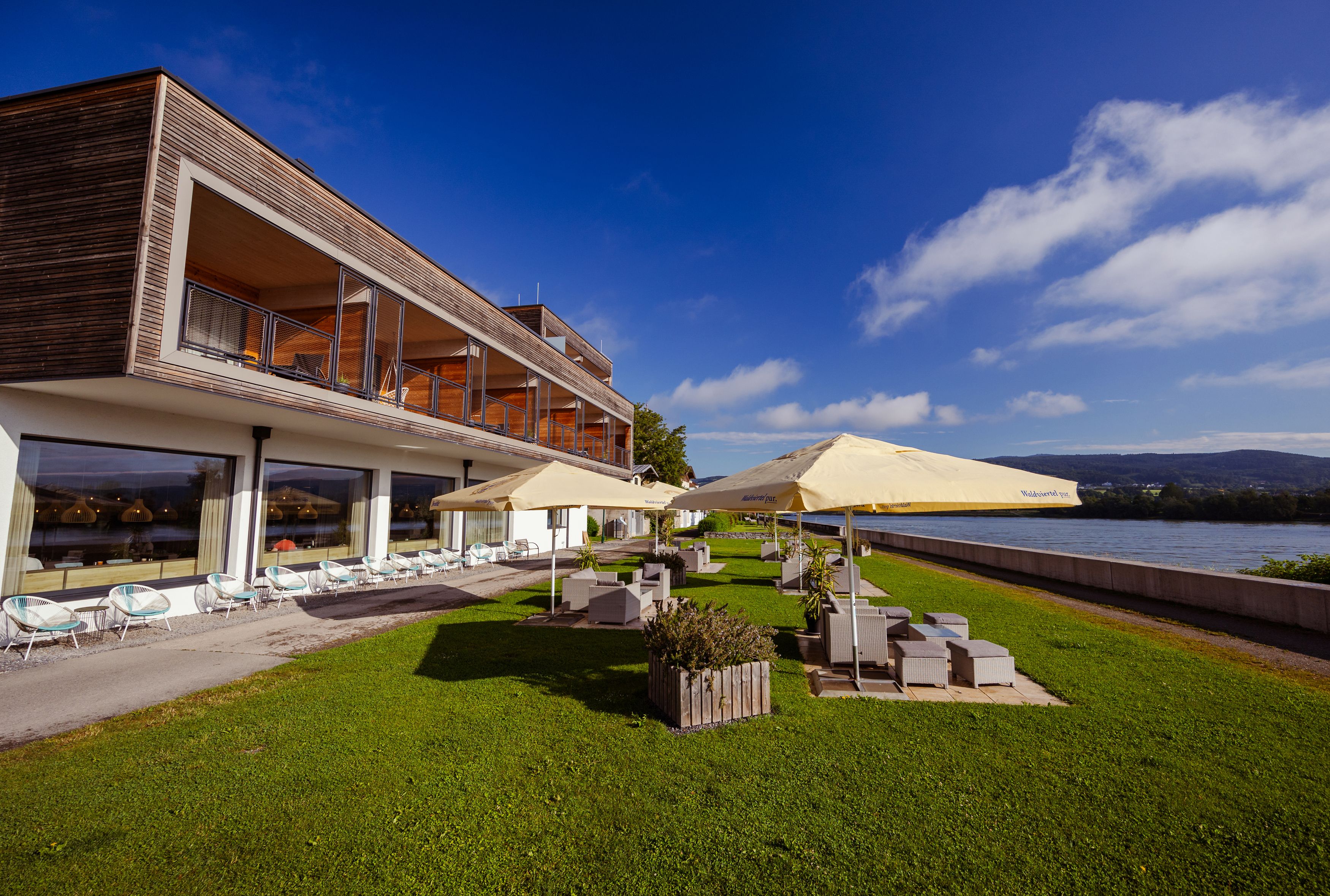 Moderne Lodge mit Terrasse und Sonnenschirmen am Flussufer.