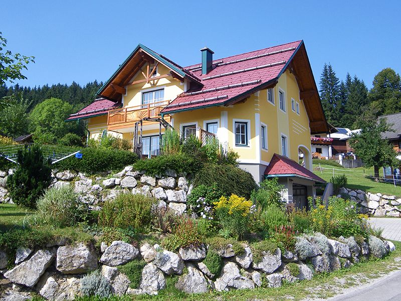 Gelbes Haus mit rotem Dach in einer grünen Landschaft.